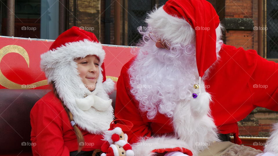 little girl dressed as father Christmas while sitting next to santa claus on his sledge.