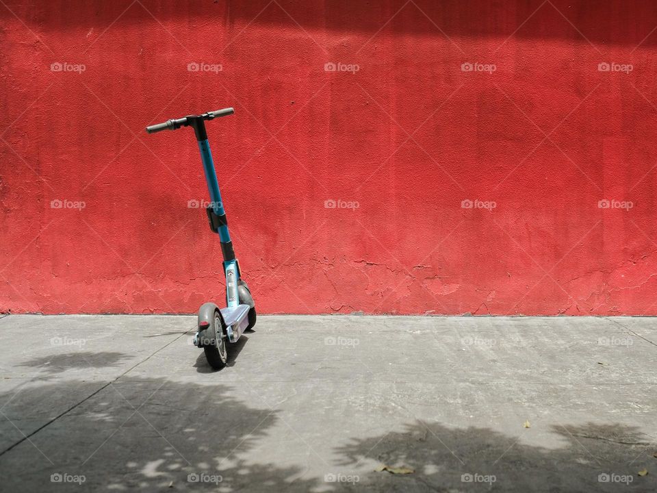 An electric scooter parked against a red wall in Kuala Lumpur, Malaysia