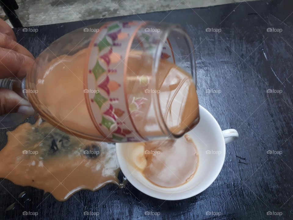 a cup of mocha coffee that was being poured but spilled over a small glass in the morning