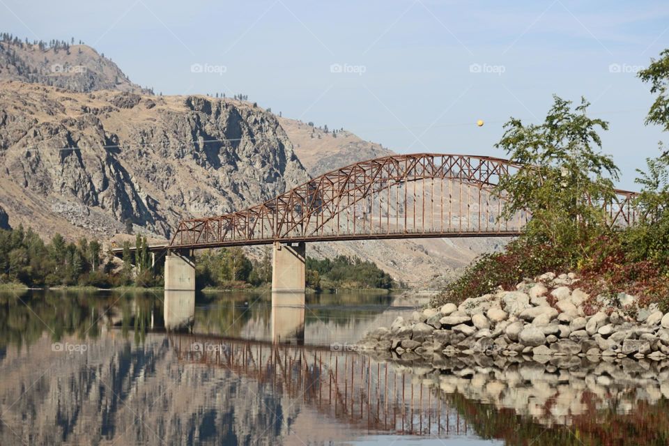 Railroad bridge and rocky cliffs reflected in the still water