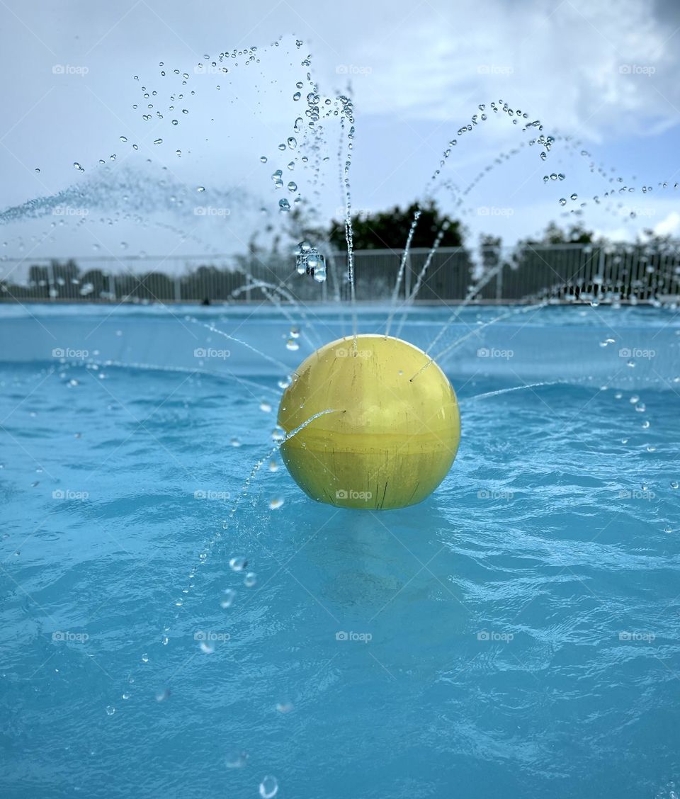 Yellow ball sending water jets into a swimming pool