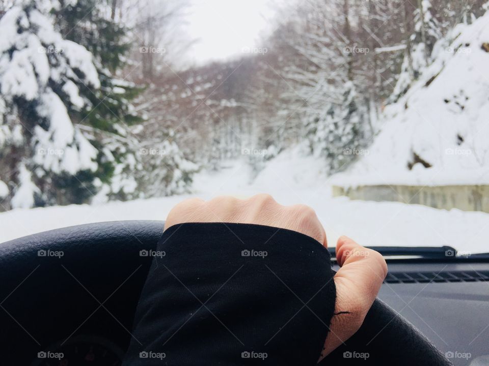 Hand on the steering wheel with snowy scenery seem through the windshield 