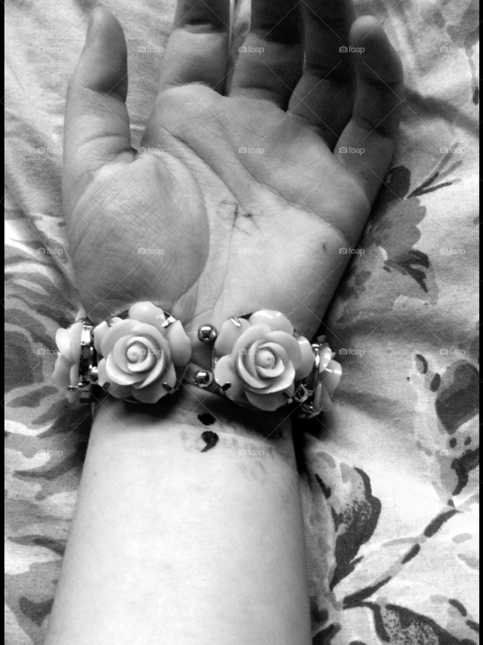 Hand . This black and white photos captures a persons arm relaxing. The emotion with the hand being still and laying lifeless gives of a sad feel. The little colon represents the semi colon project but it could represent making your career or oath choice. The rose bracelet really does make the picture beautiful and honestly if I were you I would purchase this straight away ! 