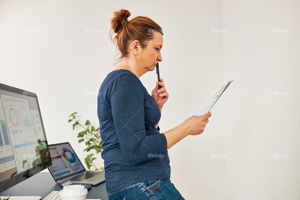 Woman entrepreneur focused on solving difficult work. Confused businesswoman thinking hard holding doccuments standing at her desk in office