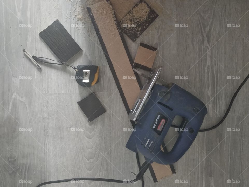Construction tools (electric jigsaw and measuring roulette) on boards in sawdust on a light wooden floor