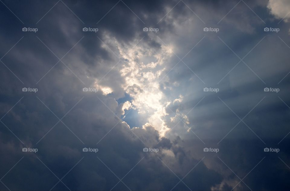 Snow white cotton candy clouds are pierced at center skyscape by radiant rays of sunlight.