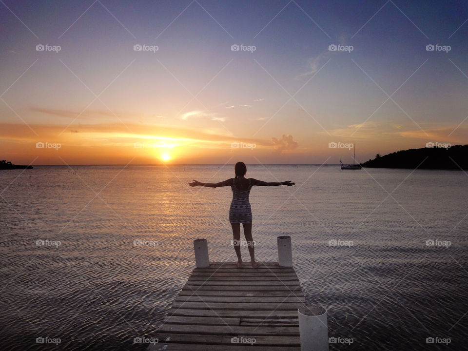 Rear view of a woman standing on pier over sea during sunset