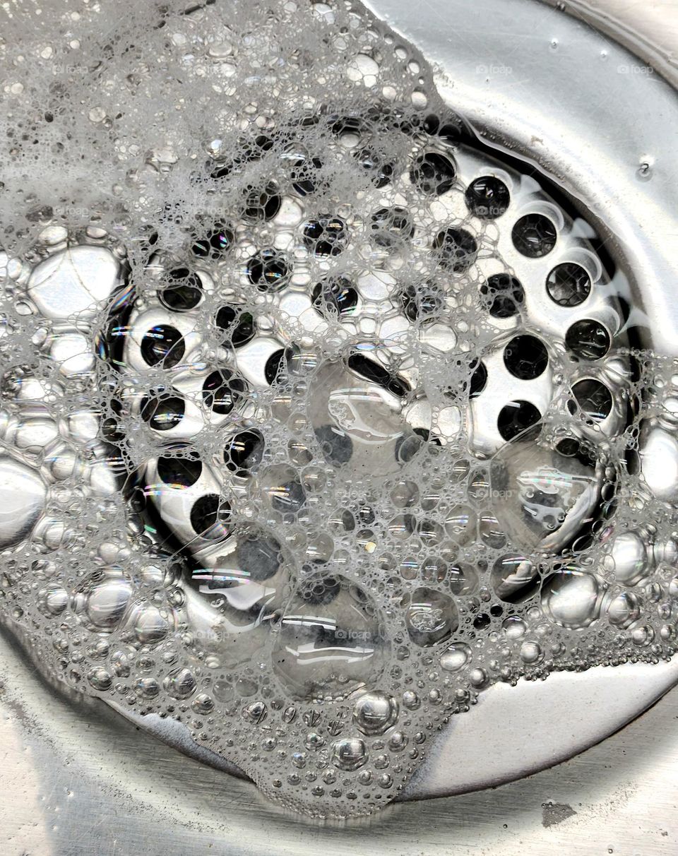 close up view of soapy bubble water going down a silver metal sink drain