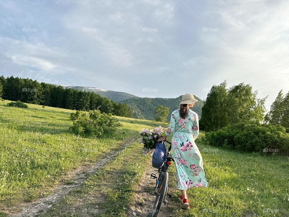 Girl in a dress with lilacs on a bicycle