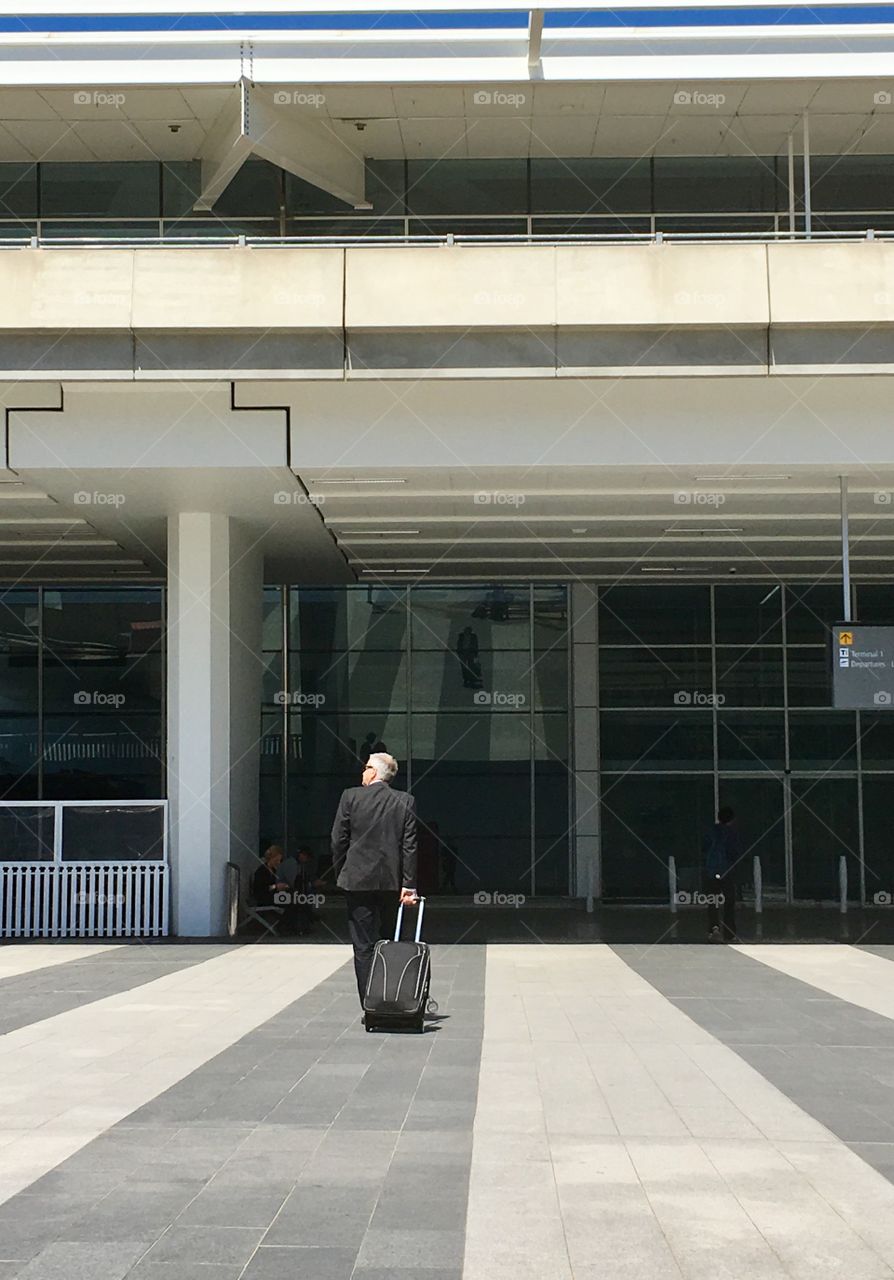 Middle aged Businessman in black suite toting carry on luggage and entering airport terminal 