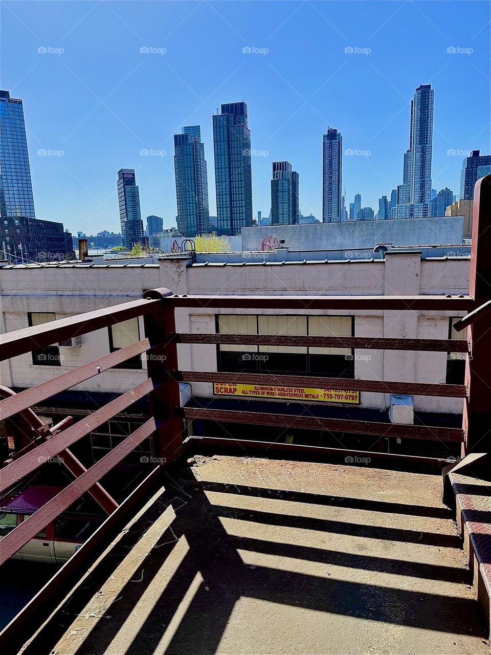 This is the middle platform of the red metal staircase of the “Pulaski Bridge” at “Newtown Creek” in LIC, Queens. The sun casts proportional shadows that combine with the actual structure to form an interesting pattern. 2024. Hypnotic Productions