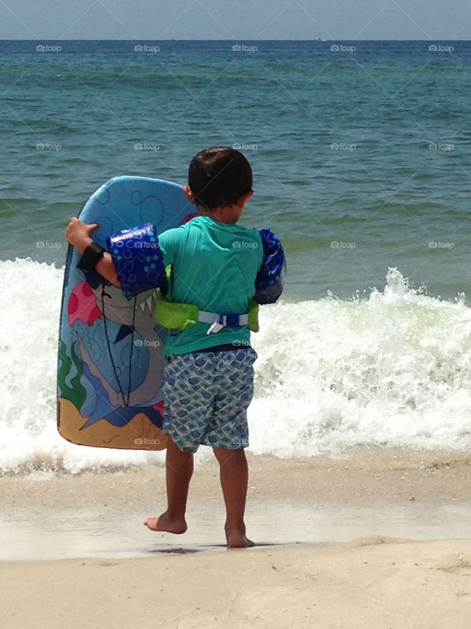 Rear view of a small boy holding surfboard