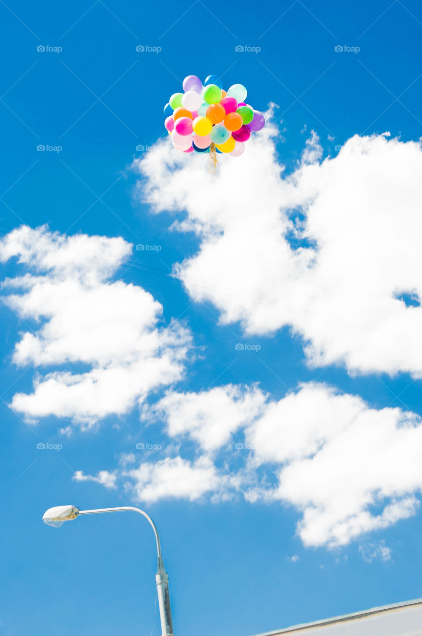 A bouquet of colorful baloons fly in the blue sky.