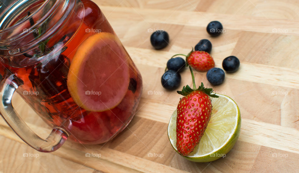 Very berry homemade lemonade with lime, organic garden strawberry, blueberry raspberry and lemon on wood background gourmet summertime drink photography