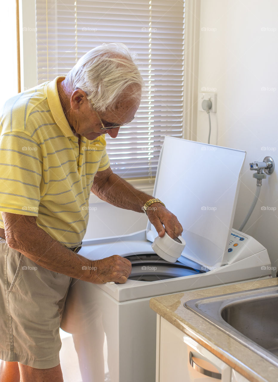 Elderly man loading his washing machine.