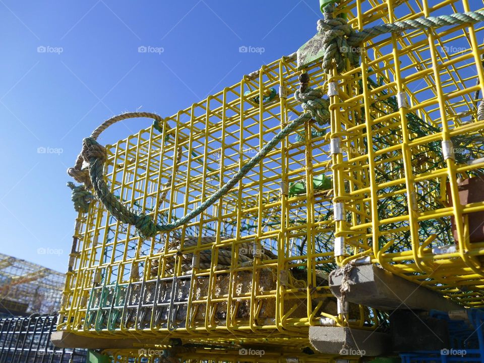 “Top Tier.”  A yellow lobster trap or “pot” on the top of a stack clashes with the noon day sun.