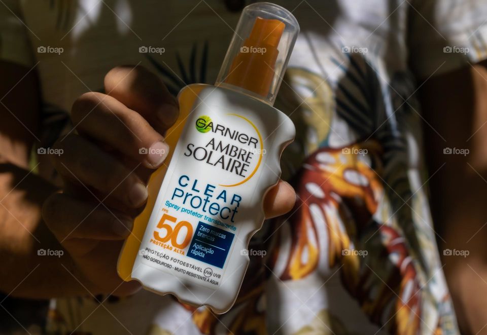 Step out of the shadows this summer with Ambre Solaris factor 50, held by a tanned man in vintage Hawaiian shirt in shadowy surroundings