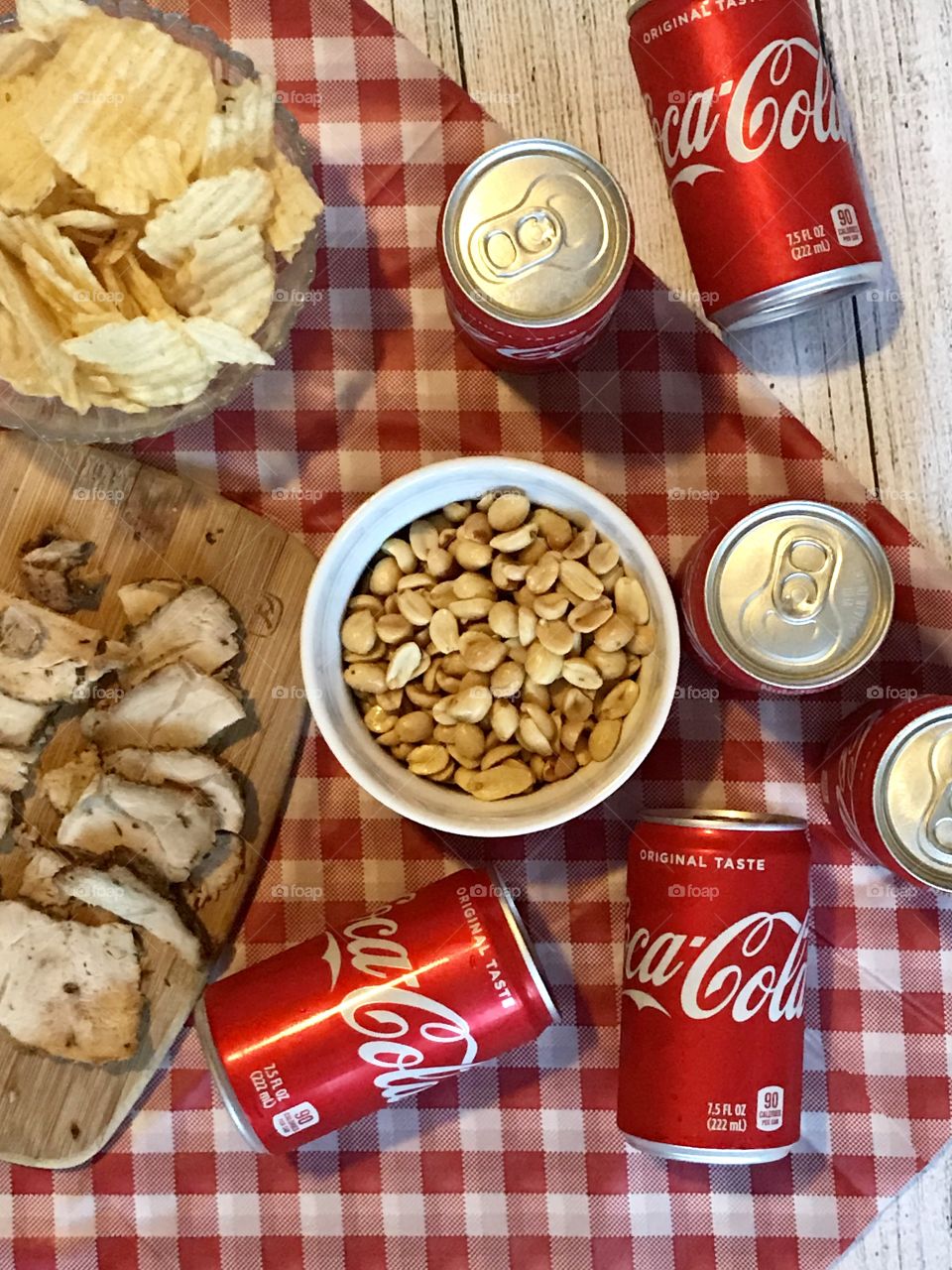Cans of Coca-Cola on a red and white checkered background with barbecue food and potato chips 