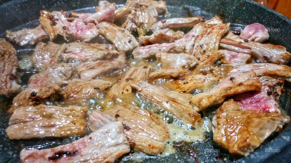 Strips of meat sizzling on a hot plate in the process of being cooked. Some raw portions are obvious.