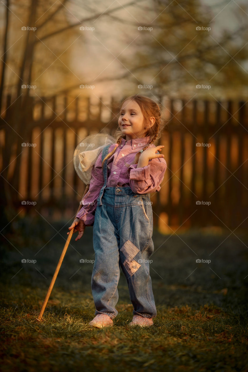 Little girl with butterfly net outdoor at sunset