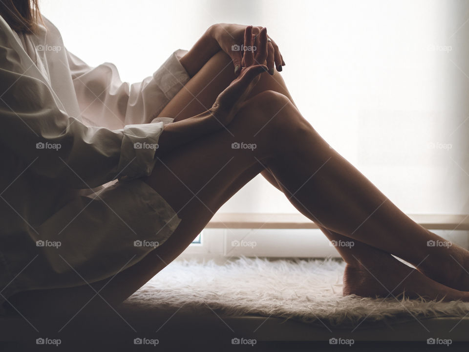 A girl in a white shirt sits on a window. Beautiful hands and feet