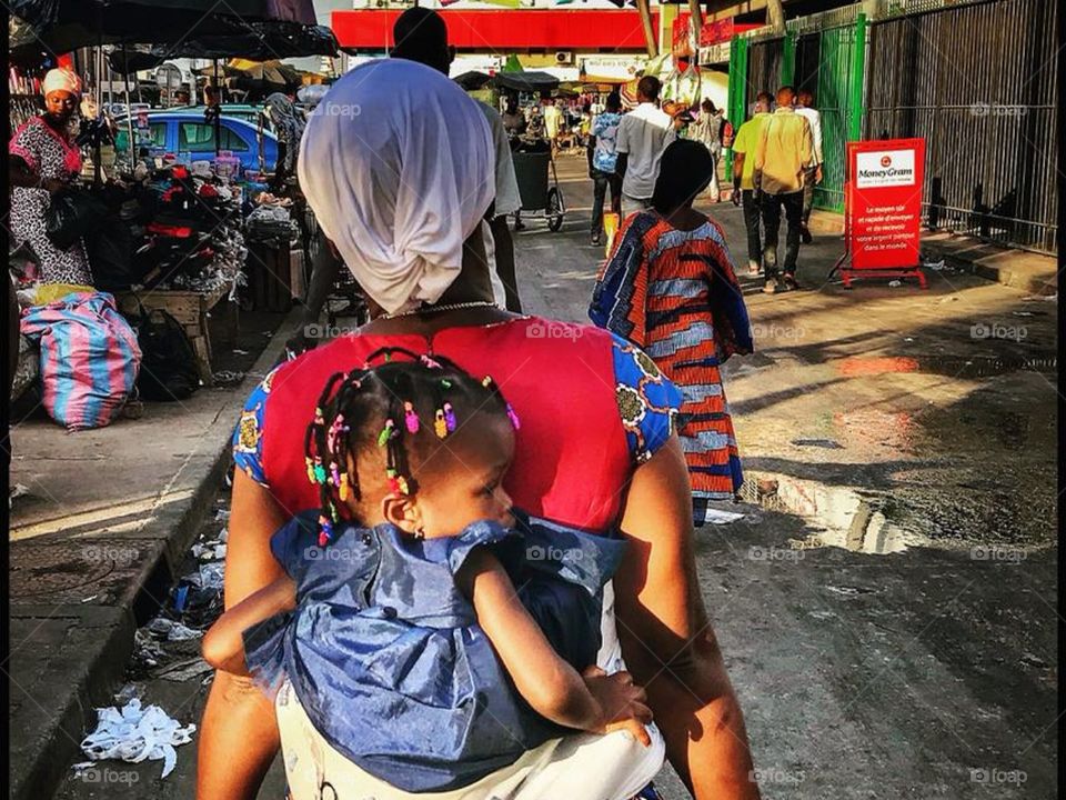 Walking in Abidjan streets. Women carrying her baby on her back.