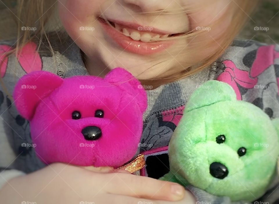 A little American girl hugging her pink and green Beanie Baby teddy bears smiling