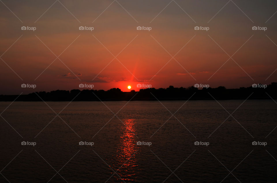 On a river boat cruise that winds down the Savannah river of Georgia a beautiful sunset descends upon the evening sky.