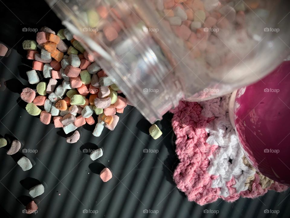 Colorful Pastel Mini Marshmallows Falling Off Clear Plastic Jar By Pink Slime Container On A Crocheted Cloth.