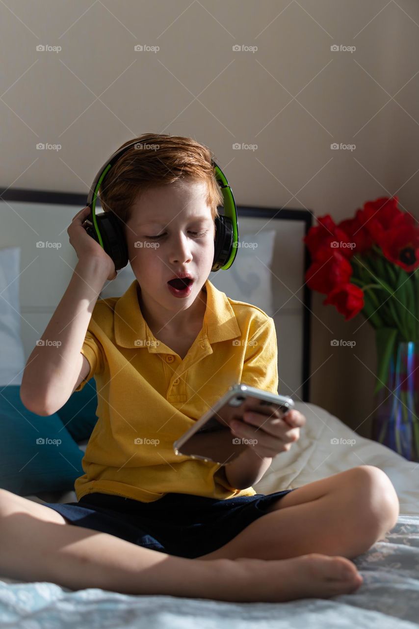 red-haired cute child boy at home on the bed in headphones listening to music