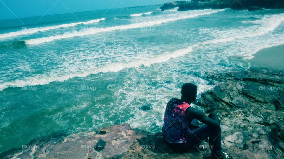 coral blue water. black man sitting by beautiful blue sea