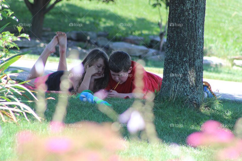 Brother and sister lying at park with mobile phone