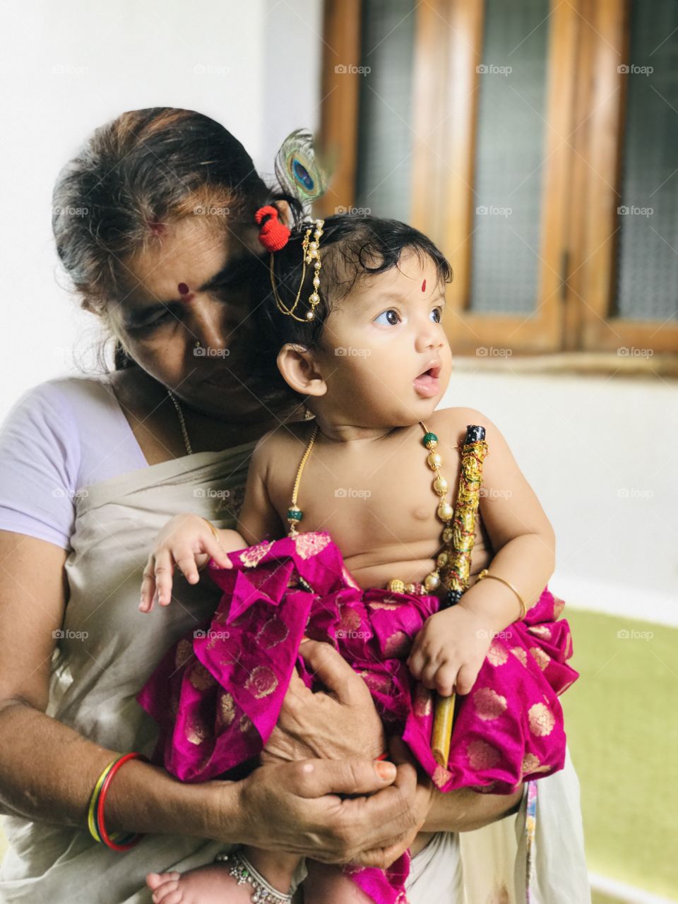 Indian baby girl wearing dress like little lord krishna and holding flute .