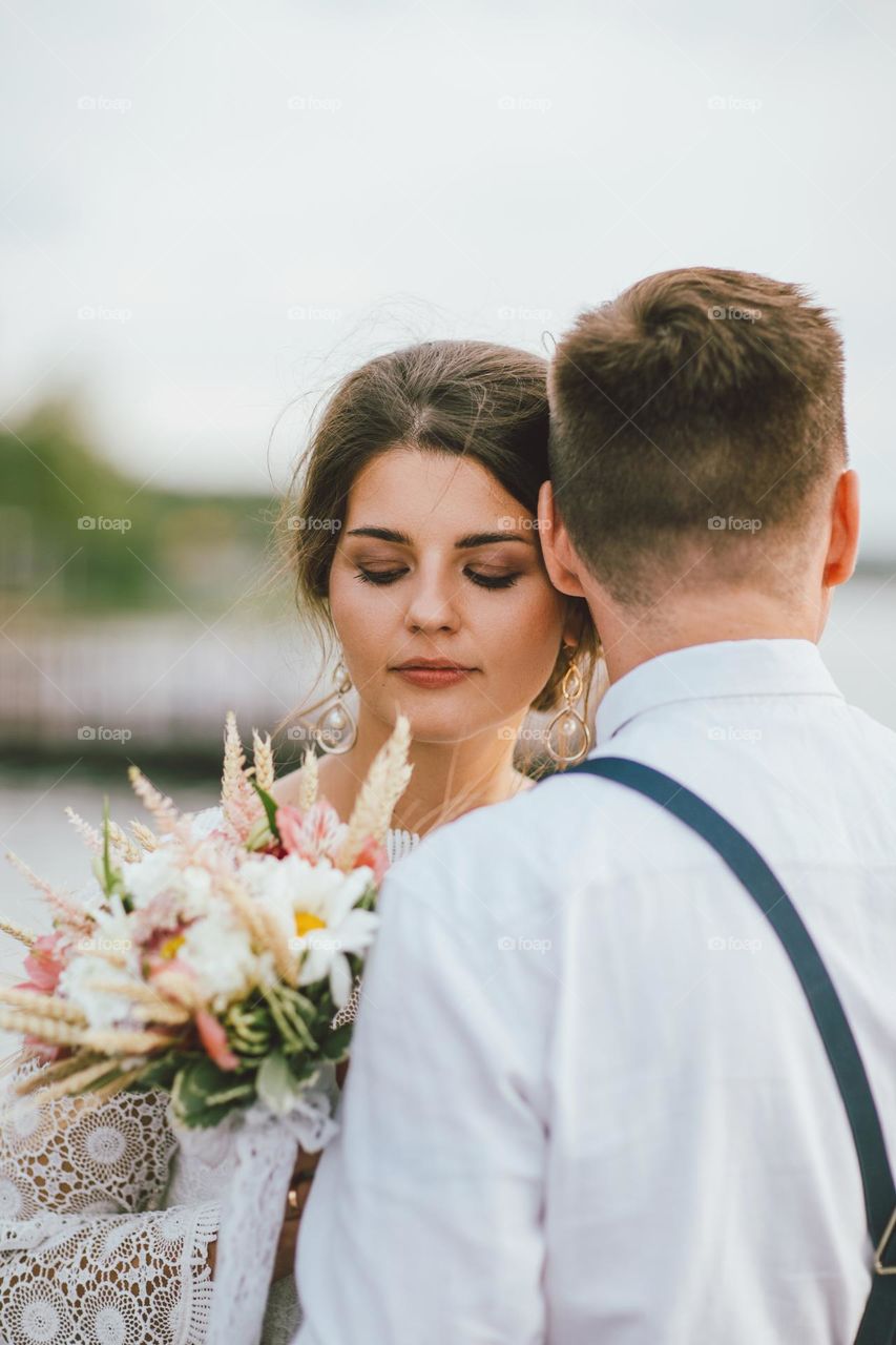 Happy newly married couple, smiling bride brunette young woman with the boho style bouquet with groom, close up portrait outdoors