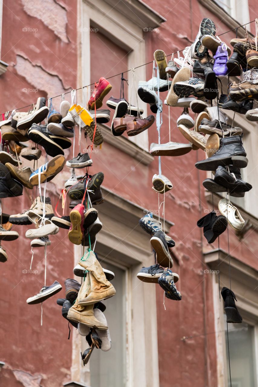 Shoes hanging from a string. Many shoes hang from the string between houses. Paint on the house is quite bad shape. Many different kind of shoes