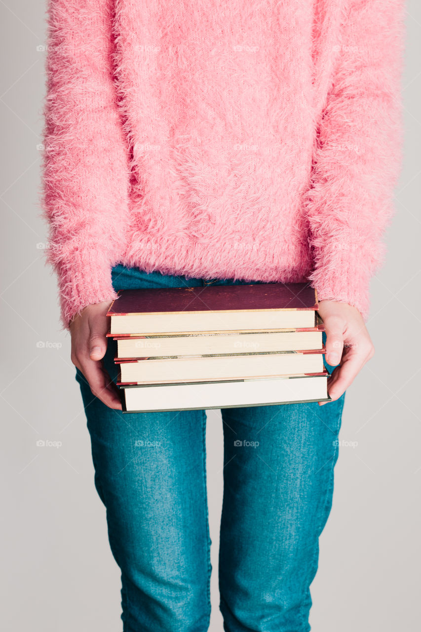 Young girl holding a few books. Teenager girl wearing pink sweater and blue jeans. Vertical photo