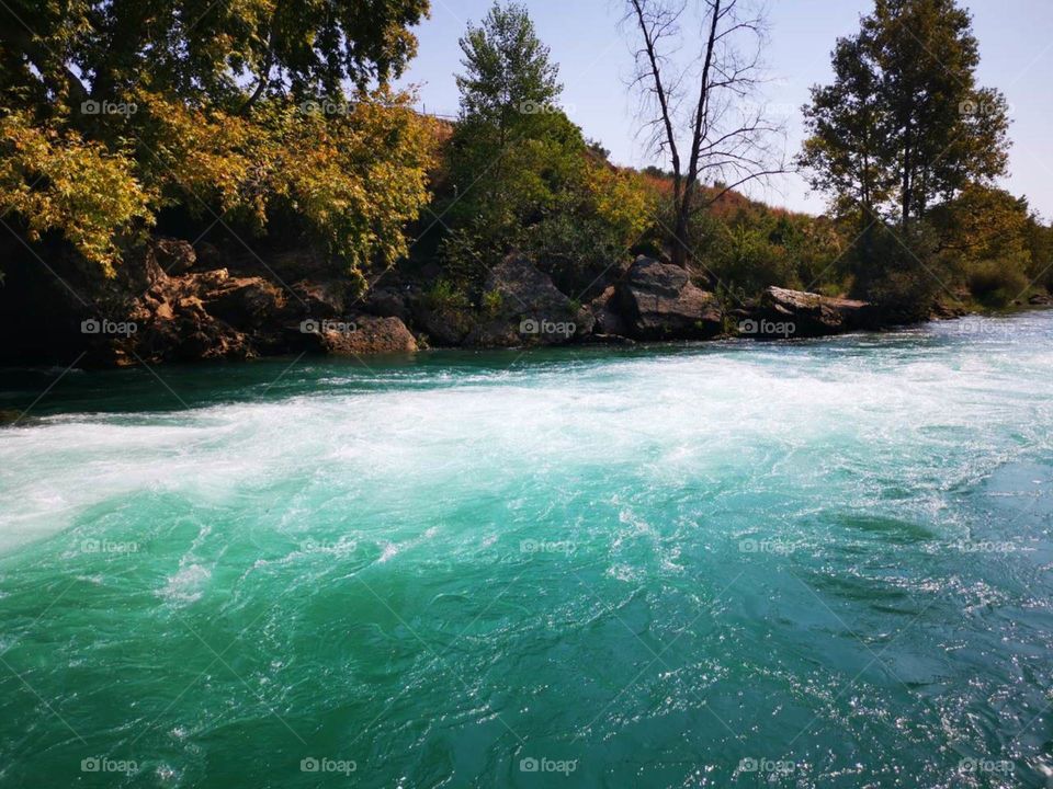 A beautiful white stream of the turquoise blue river from the waterfall. With green and yellow autumn nature.