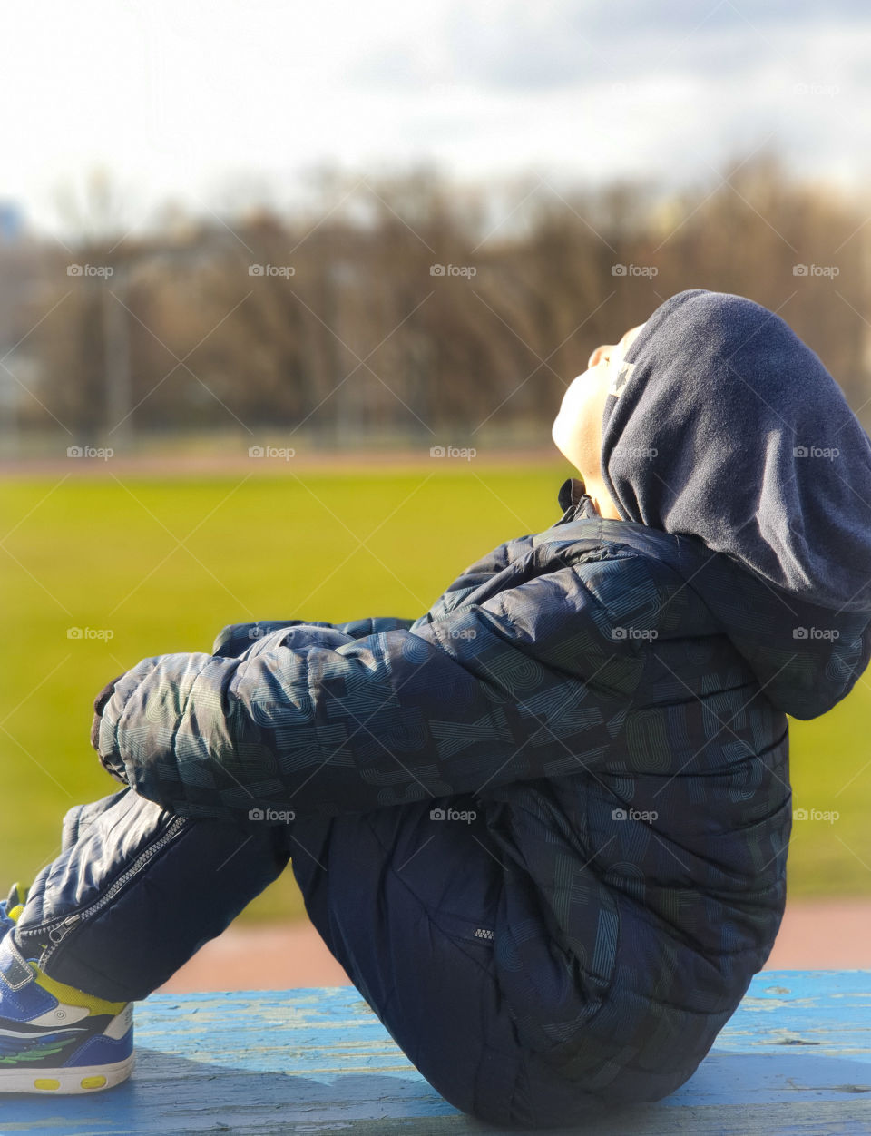 Spring sunny day, a boy sitting in a stadium in the park enjoys the spring warmth, set his face to the sun's rays