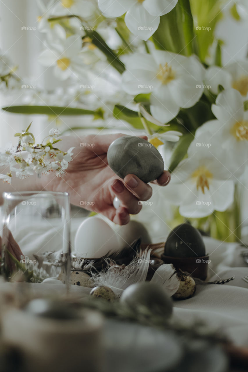 Girl is holding a grey dyed egg on a served Easter table with flowers