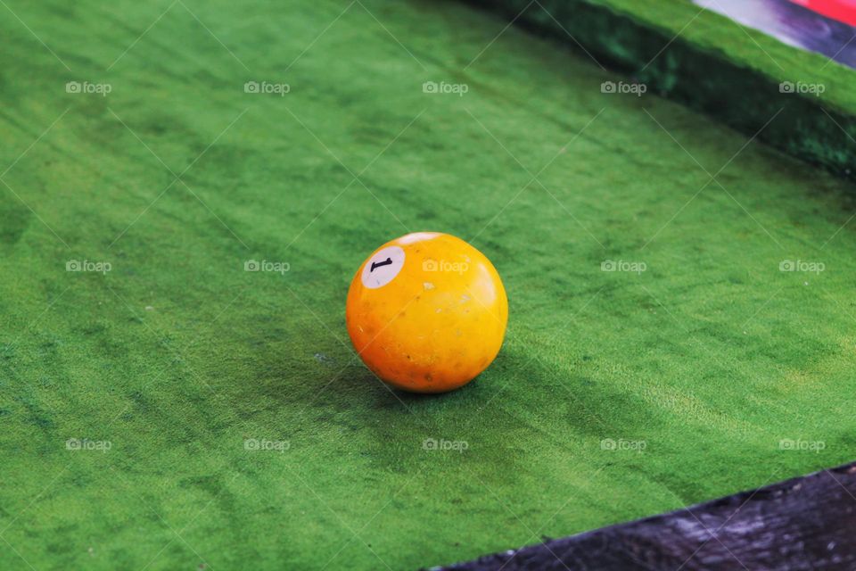 an orange billiard ball with the number one on its side lies on a green cloth