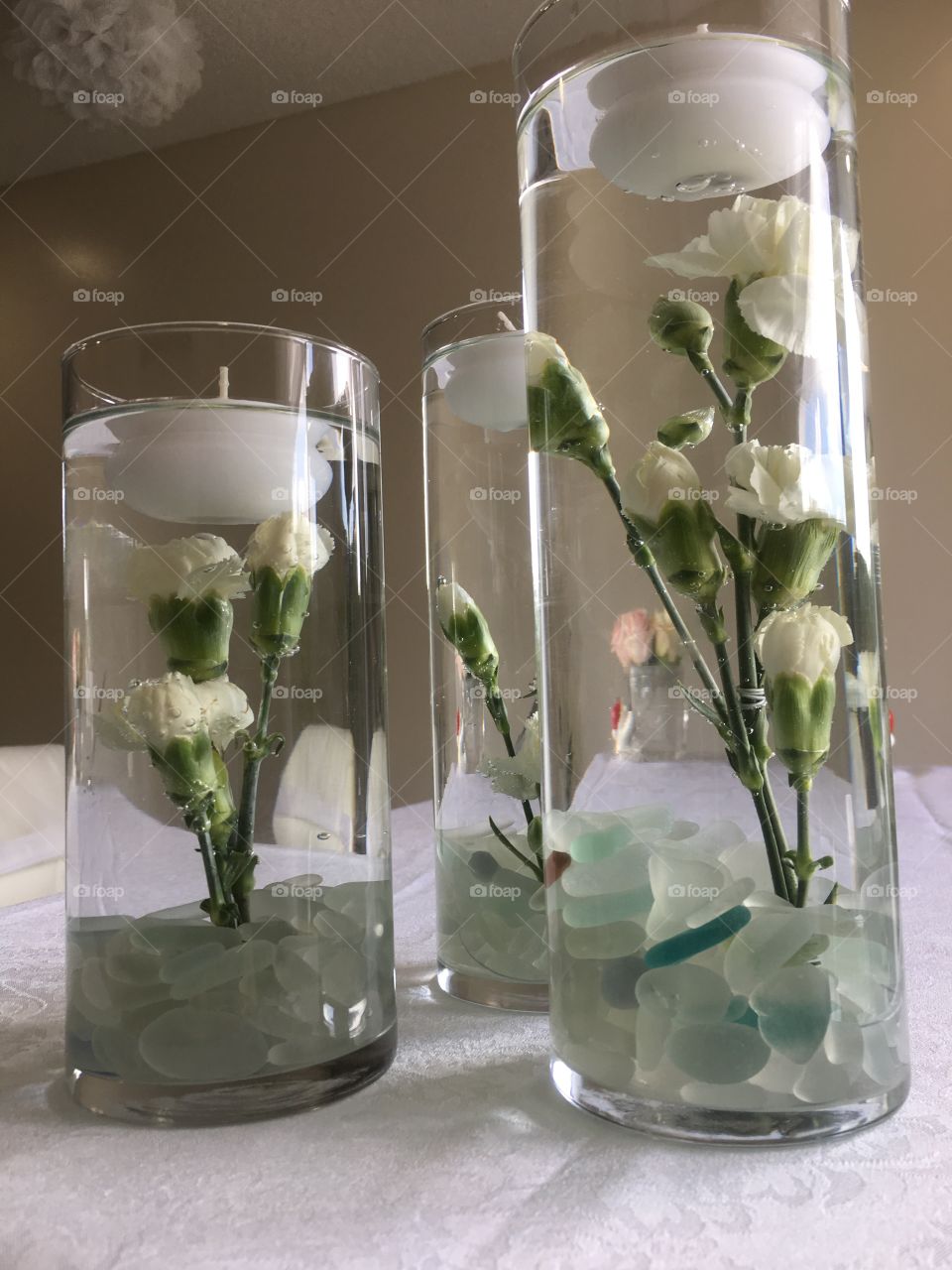 Close up of the beautiful white flowers and candles in water used as wedding decorations. The base of the vase is filled with mainly clear beach glass found while on vacation in Jamaica 