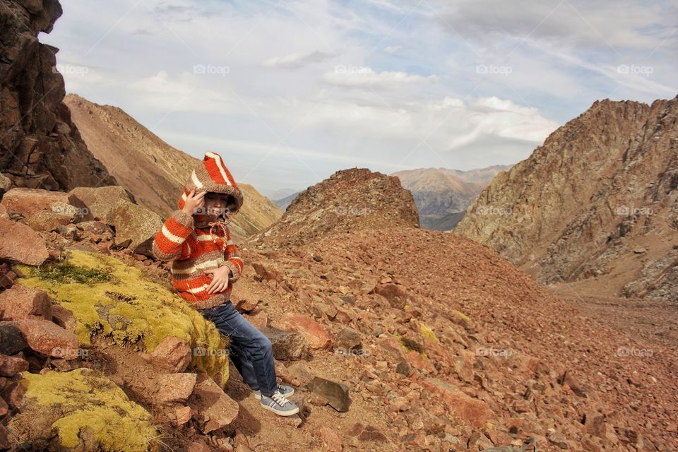 A girl in a knitted jacket is resting while sitting on a perennial moss in the mountains on a glacier