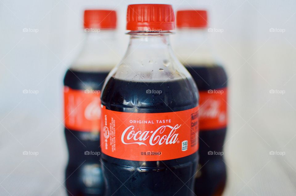 Three plastic bottles of Coca-Cola on a white rustic background