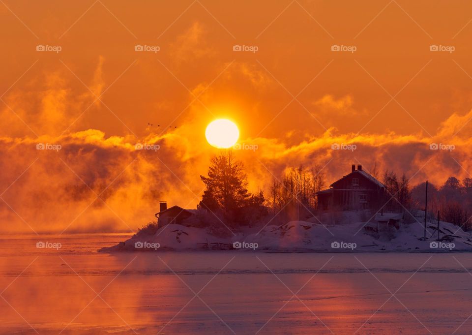 Small traditional cottage on an icy island in the archipelago of Helsinki, Finland at sunrise on an extremely cold winter morning.