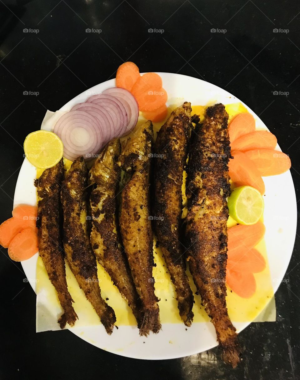 Delicious Indian fish fry garnished with slice onions carrots and lemon 