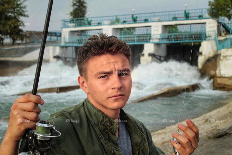 portrait of a young fisherman on the background of a river dam