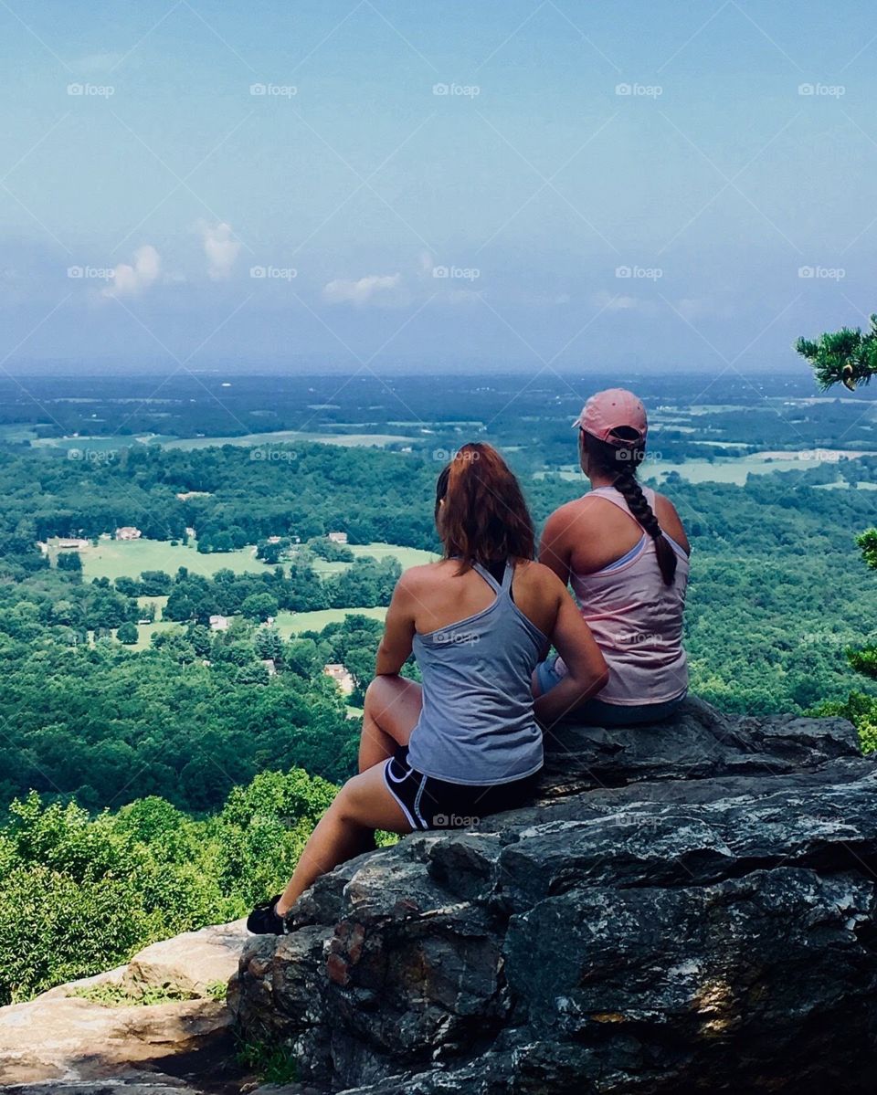 2 girls staring out over mountain overlook at the green trees
