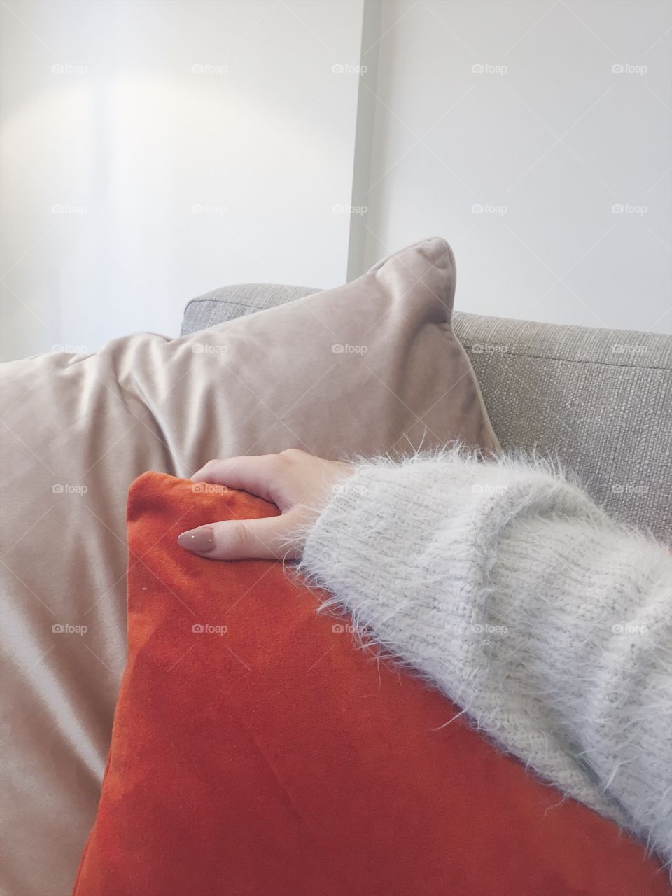Female with pink nails holding an orange terracotta cushion on a couch