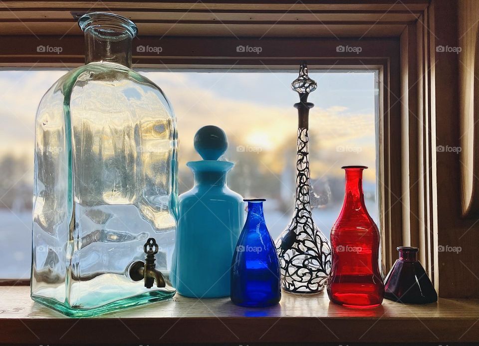 A hand blown glass jug distorts the fading winter light that illuminates a spectrum of colored bottles.