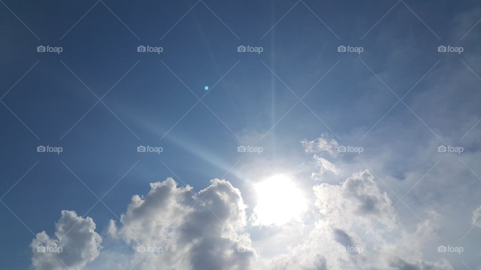 Bright sun with rays on blue sky with clouds